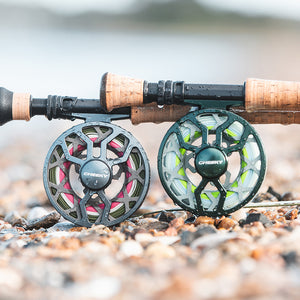Two cheeky drip fly fishing reels side by side on rocks