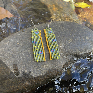 Handmade beaded earrings resting on a rock beside flowing water.