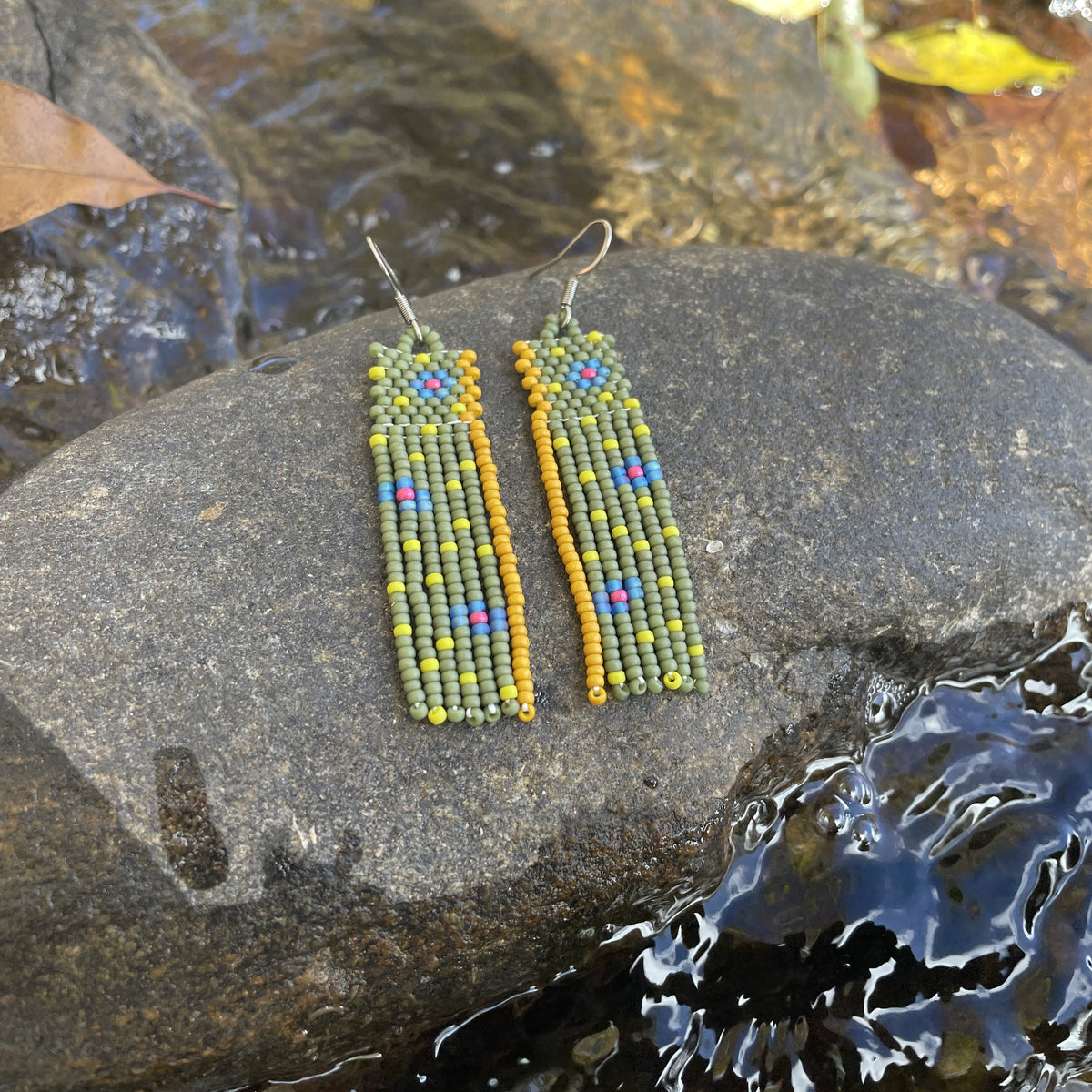 Handmade beaded earrings resting on a rock beside flowing water.